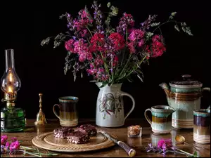 Bukiet kwiatów obok lampy, serwisu do kawy i ciasta