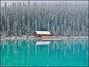 Dom pod ośnieżonym lasem nad jeziorem Louise Lake w padającym śniegu