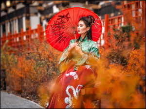 Azjatka z parasolką na tle jesiennych krzewów