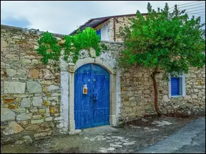 Drzewo przy kamiennym domu z niebieską bramą