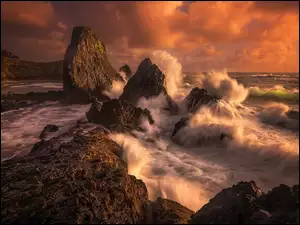 Zachód słońca nas morskimi falami z skałami