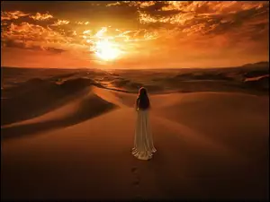 Kobieta na pustyni spogląda na zachodzące słońce