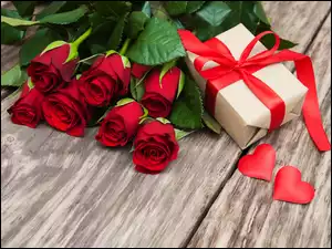 Serduszka i prezent przewiązany wstążką obok bukietu czerwonych róż