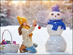 Dziewczynka z koszem ozdób i bałwankiem w śniegu