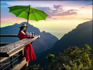Kobieta pijąca kawę pod zieloną parasolką na tarasie widokowym
