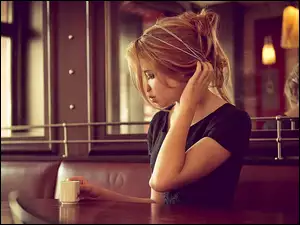 przy stole siedząca dziewczyna z kubkiem kawy z odbiciem w lustrze