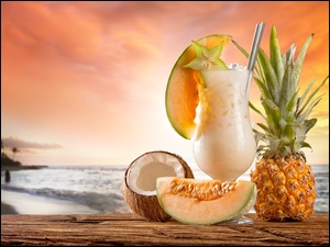 Ananas oraz cząstka melona i kokosa obok koktajlu w szklance z widokiem na morze