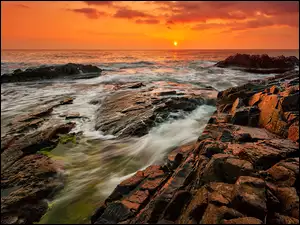 Zachód słońca nad kamienistym brzegiem morza