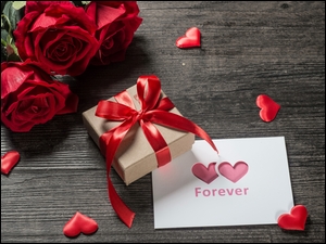 Czerwone róże położone obok prezentu i kartki z sercami
