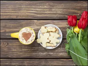 Kawa i ciasteczka na talerzyku obok tulipanów