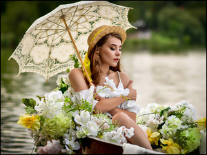 Dziewczyna z parasolem i kapeluszem w łodzi z kwiatami