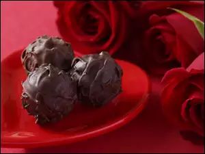 Pralinki na talerzyku w kształcie serca obok róż