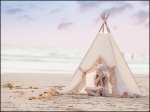 Dziewczynka przed namiotem na plaży słucha morskich fal z muszli
