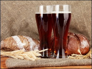 Kwas chlebowy w szklankach obok bochenków chleba i kłosów zboża