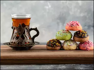 Szklanka herbaty i kolorowe pączki na desce