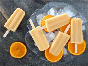 Lody na patykach położone na plasterkach pomarańczy