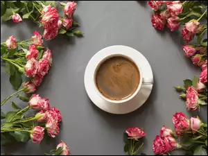 Róże ułożone wokół filiżanki z kawą