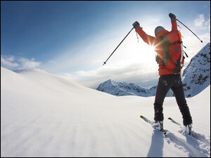 Promienie słońca muskają szczęśliwego narciarza na tle gór pokrytych śniegiem