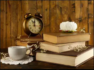 Biała piwonia na książkach obok zegara i filiżanki