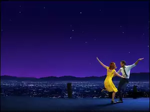 Aktorzy Emma Stone i Ryan Gosling tańczą nocą na tle panoramy miasta