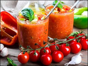 Pomidory na gałązce obok szklanek z sokiem z pomidorów