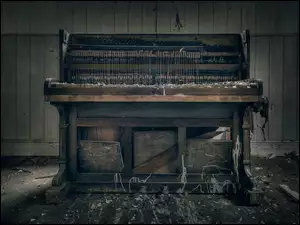 pod drewnianą ścianą stoi stare pianino