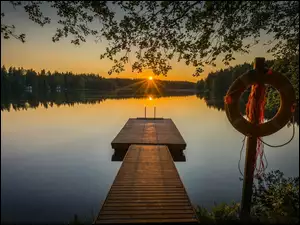 Kolo ratunkowe pod drzewem i pomost na jeziorze w blasku zachodzącego słońca