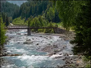 Most na rzece i drzewa po obu stronach rzeki z górami w tle
