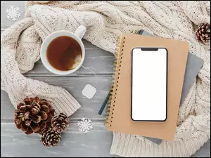 Obok kubka z herbatą notes z telefonem na swetrze