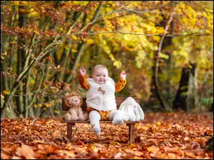 Dziewczynka na ławce pośród pluszowych maskotek w jesiennym parku
