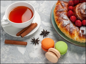 Filiżanka herbaty obok makaroników i ciasta z truskawkami
