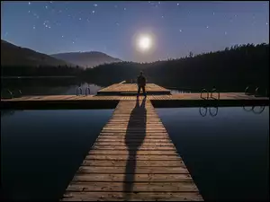 Mężczyzna na pomoście nad jeziorem w blasku księżyca