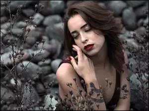 Szatynka z tatuażem na ręce pośród roślin