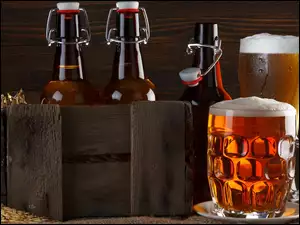 Skrzynka z butelkami obok kufli napełnionych piwem
