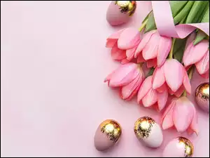 Pozłacane jajka obok różowych tulipanów ze wstążką