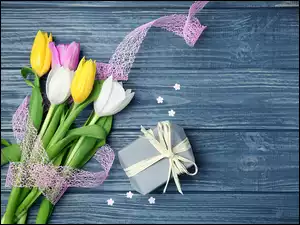 Mały prezent i kolorowe tulipany ze wstążką na niebieskich deskach