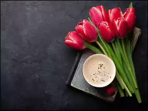 Filiżanka kawy obok zroszonych czerwonych tulipanów na ciemnym tle