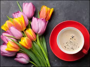 Kawa w czerwonej filiżance obok kolorowych tulipanów