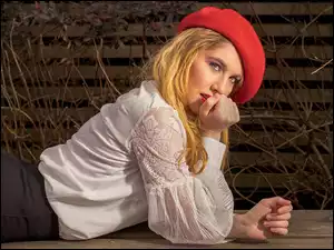 Leżąca na deskach kobieta w białej bluzce i czerwonym berecie
