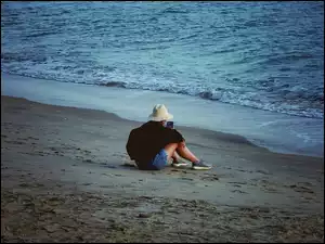 Nad brzegiem morza siedząca dziewczyna w kapeluszu