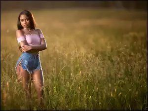 Ciemnoskóra dziewczyna w krótkich spodenkach i w bluzce wśród trawy na łące