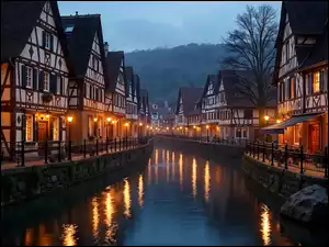 Zapalone latarnie przed domami nad kanałem w zapadającym zmroku