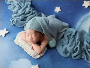 Śpiący noworodek na tkaninie z gwiazdkami w niebieskiej czapeczce z pomponem
