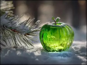 Zielone szklane jabłko na śniegu obok ośnieżonych gałązek sosny