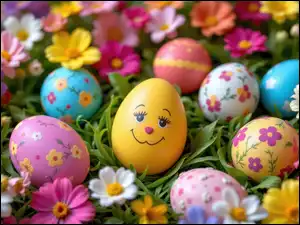 Uśmiechnięte jajko wśró kolorowych pisanek i kwiatów na trawie